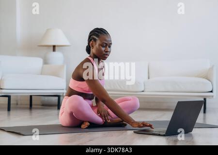 Prendre des leçons en ligne en utilisant un ordinateur portable. La femme fait du yoga à la maison. Banque D'Images