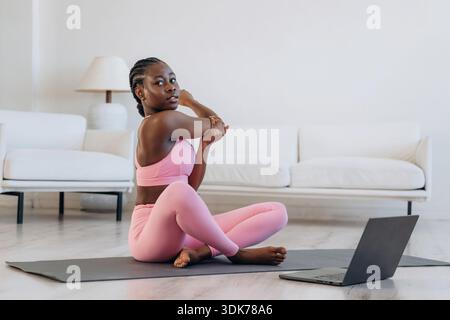Prendre des leçons en ligne en utilisant un ordinateur portable. La femme fait du yoga à la maison. Banque D'Images