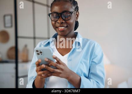 Médias sociaux, debout et tenant smartphone. La femme est à la maison dans la chambre domestique. Banque D'Images