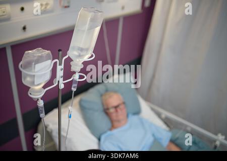 Homme âgé au repos dans un lit d'hôpital sous traitement intraveineux Banque D'Images
