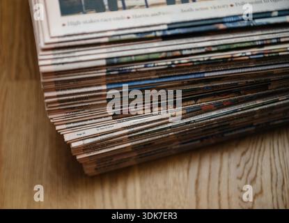 Vue rapprochée de journaux empilés reposant sur une surface en bois montrant les titres de pages superposés et la texture de l'impression symbolisant les informations journalistiques des médias d'information Banque D'Images