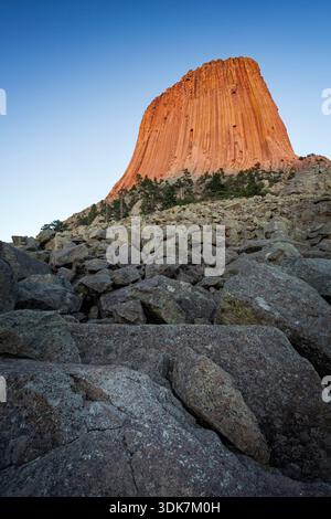La tour du diable brille orange dans la lumière du soir, s'élevant au-dessus des pentes rocheuses et des pins dans le nord-est du Wyoming. Banque D'Images