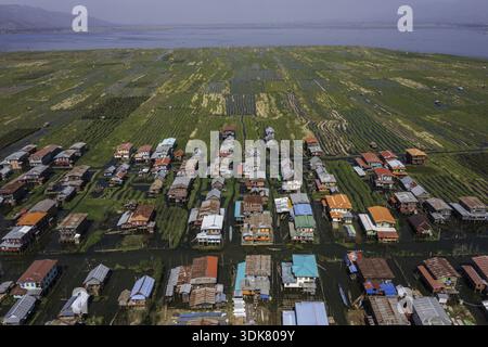 Vue aérienne de maisons sur pilotis avec des toits colorés s'élèvent de l'eau au milieu de jardins flottants sous un large ciel, Myayni Gone, Shan, Myanmar. Banque D'Images