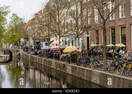 Dîner en plein air le long d'un canal à Delft, une ville hollandaise. Beaucoup de gens assis dehors appréciant la nourriture et les boissons Banque D'Images