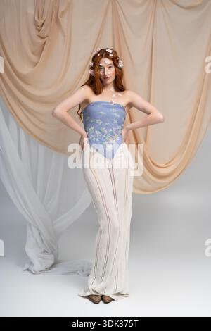 Une jeune femme rousse pose gracieusement dans une tenue florale avec des fleurs de printemps fraîches. Banque D'Images