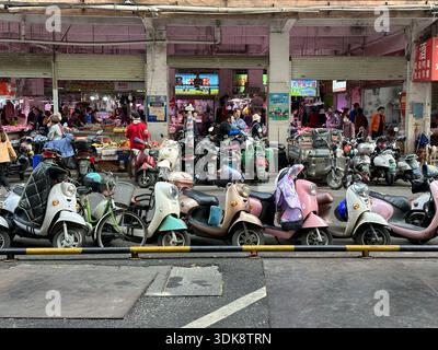 Nanning, Chine - 7 janvier 2024 : scène de marché de rue animée avec de nombreux scooters garés et des gens faisant du shopping en Chine. Banque D'Images
