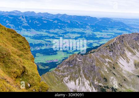 Une vue panoramique depuis une crête de haute montagne révèle des pentes abruptes herbeuses et rocheuses au premier plan, descendant brusquement vers une large vallée en contrebas. Le Banque D'Images