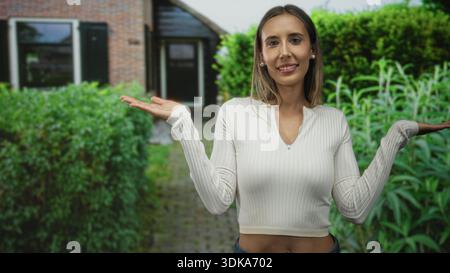 Femme avec les paumes levées et les mains tendues, les yeux fermés et un léger sourire, portant un pull côtelé et un Jean à l'entrée du bâtiment ; équilibre de sérénité. Banque D'Images