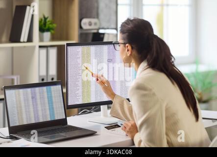 Comptable femme analysant les données de tableur sur les écrans d'ordinateur dans le bureau moderne Banque D'Images