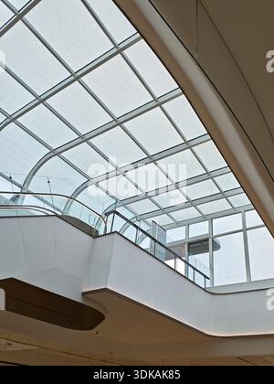 Vue intérieure en angle bas d'un bâtiment blanc moderne aux murs incurvés et au toit vitré grillagé laissant pénétrer la lumière naturelle Banque D'Images