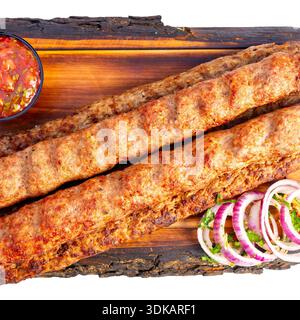 Les kebabs sont servis sur une planche de bois avec des oignons frais, de la coriandre et un petit bol de sauce. Ce repas a l'air savoureux et frais. Banque D'Images
