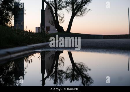 Vue horizontale à faible angle d'une flaque d'eau de bord de route reflétant la silhouette d'arbres et de bâtiments éloignés contre un ciel nocturne spectaculaire. Banque D'Images
