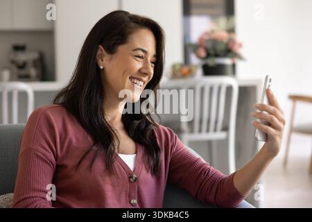 Femme attrayante assise sur un canapé avec smartphone Banque D'Images