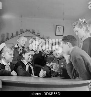 Slaviansk, RSS d'Ukraine, Union soviétique, années 1960 Une photographie d'archives montrant une leçon d'orientation professionnelle ou une réunion d'un club d'aviation. Un officier soviétique et héros de l'Union soviétique montre un modèle d'avion à un groupe de pionniers. La salle de classe est équipée de modèles géométriques sur les étagères, suggérant un accent sur les sciences techniques ou les mathématiques. Les enfants écoutent attentivement les histoires du vétéran sur le ciel. Cette image capture l'esprit de mentorat et le prestige de la profession militaire dans le Donbass pacifique. Banque D'Images