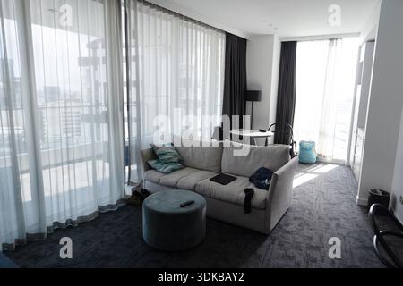 Intérieur d'une chambre d'hôtel moderne avec coin salon et grandes fenêtres donnant sur la ville à Auckland, Nouvelle-Zélande. Banque D'Images