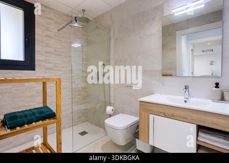 Salle de bains contemporaine avec douche en verre, meuble-lavabo flottant et carrelage beige au design épuré Banque D'Images