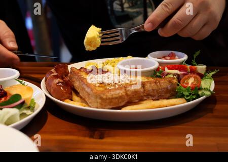 Petit-déjeuner traditionnel avec œufs brouillés, pain grillé et saucisses sur une table en bois Banque D'Images