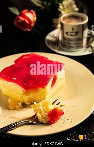Une tranche de dessert rose est sur une assiette blanche à côté d'une tasse à café. Le dessert est coupé en deux et une fourchette en sort Banque D'Images