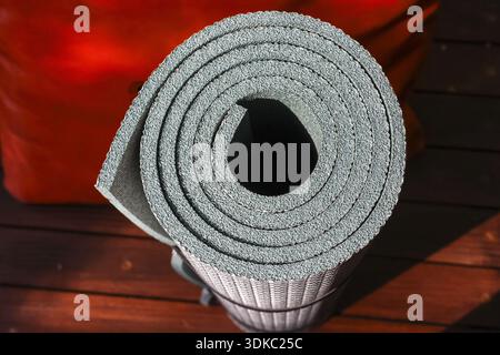 Coussin de couchage en mousse grise roulée pour le camping, équipement de plein air essentiel pour le confort et le repos. Ce tapis sur fond en bois inspire le sentiment de la prépara Banque D'Images