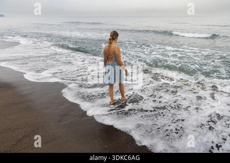 Jeune femme marchant sur la plage de sable noir à Lovina, Bali, Indonésie Banque D'Images