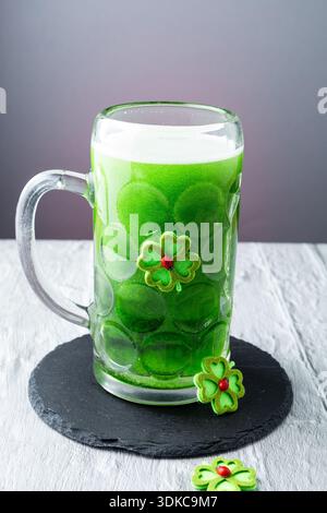 Bière verte versée dans une tasse en verre décorée de trèfle pour la fête de la Saint Patrick. Concept festif de bière irlandaise avec mousse, mouvement et c Banque D'Images