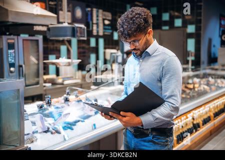 Bloc-notes noir dans les mains. Le travailleur masculin est dans l'épicerie. Banque D'Images