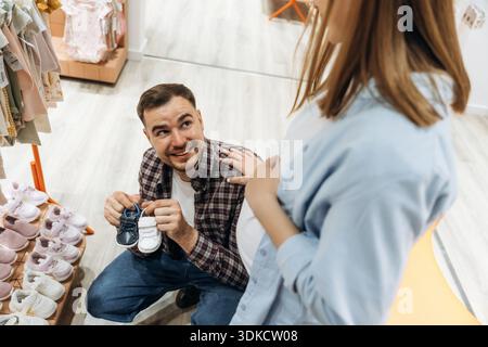 Petites chaussures mignonnes. Femme enceinte avec homme sont dans le magasin de vêtements pour enfants. Banque D'Images