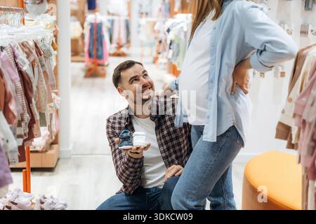 Petites chaussures mignonnes. Femme enceinte avec homme sont dans le magasin de vêtements pour enfants. Banque D'Images