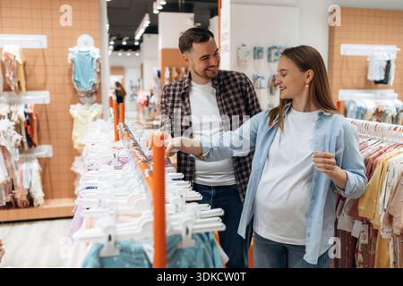 Expressions faciales positives. Femme enceinte avec homme sont dans le magasin de vêtements pour enfants. Banque D'Images