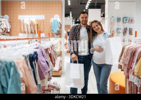 Expressions faciales positives. Femme enceinte avec homme sont dans le magasin de vêtements pour enfants. Banque D'Images