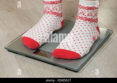 Pieds dans des chaussettes de Noël confortables debout sur des balances de salle de bain numériques, concept de résolution du nouvel an Banque D'Images