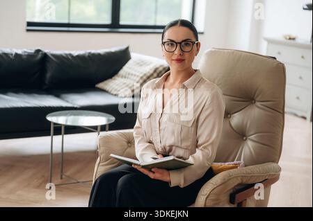Détente sur la chaise, assis. Femme en vêtements formels est dans la grande pièce moderne. Banque D'Images