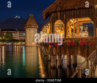 Le pont de la chapelle à Lucerne, en Suisse, est illuminé au crépuscule. Le pont historique en bois, orné de fleurs, enjambe la rivière Reuss, avec le W. Banque D'Images