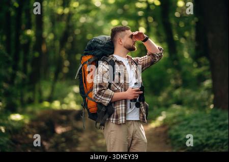 Vue latérale, debout, tenant des jumelles. Touriste masculin est avec sac à dos dans la forêt. Banque D'Images