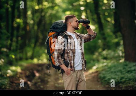 Vue latérale, debout, tenant des jumelles. Touriste masculin est avec sac à dos dans la forêt. Banque D'Images