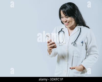 Médecin asiatique souriant à l'aide d'un smartphone isolé. Jeune médecin féminin asiatique utilisant le téléphone, travailleuse de santé féminine tenant le téléphone portable Banque D'Images