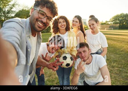 Selfie Time, souriant. Les jeunes amis s'amusent sur le terrain avec le ballon de football. Banque D'Images