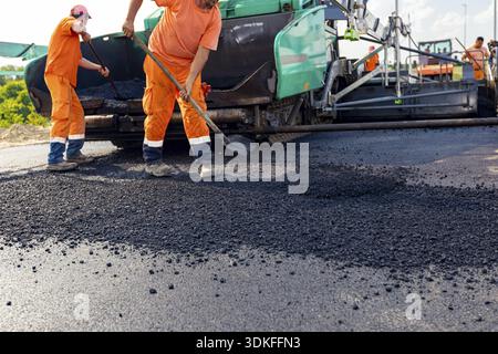 Vue sur la machine pour la pose d'asphalte, l'épandage de couche de tarmac chaud sur un sol préparé quelques travailleurs utilisent des pelles pour le niveler Banque D'Images