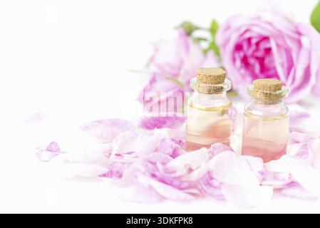 Deux flacons d'huile essentielle de rose, de roses roses et de pétales de rose isolés sur fond blanc Banque D'Images