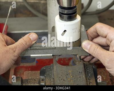 Gros plan du travailleur en tenant les mains de machiniste une mesure du diamètre de coupe du trou dans un morceau de métal à l'aide de compas Banque D'Images