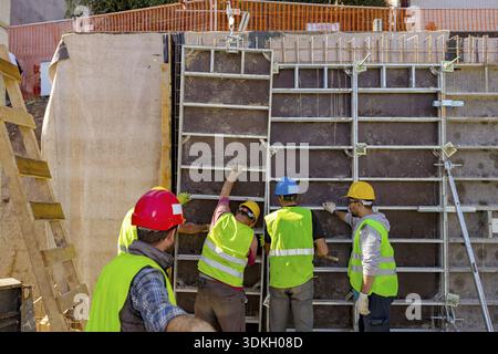 Vue de derrière sur le superviseur en supervisant l'équipe de travailleurs de la construction avec gilet de sécurité et casques jaunes pendant qu'ils assemblent manuellement de haut bois de Banque D'Images
