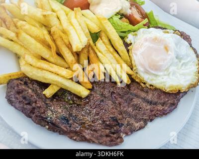 Pavé de boeuf servi avec des œufs frits, des frites et de la salade sur une table de restaurant Banque D'Images