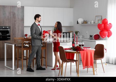 Couple aimant échangeant des cadeaux près de la table à manger servie à la maison. Célébration de la Saint-Valentin Banque D'Images