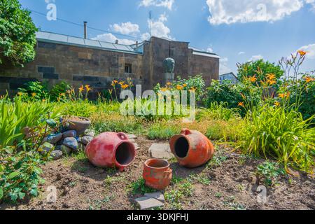 Pots traditionnels en argile placés dans une cour de jardin ensoleillée avec des fleurs et de la verdure à Gyumri, Arménie. Banque D'Images
