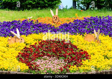 Parterre de fleurs coloré de pansies et de marguerites décorées avec des lapins de Pâques en bois dans le parc au printemps Banque D'Images