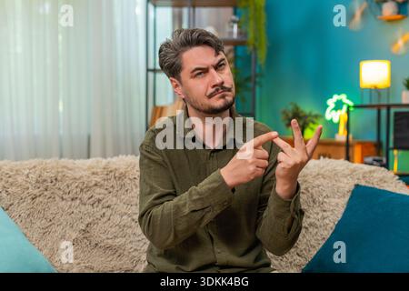 L'homme d'âge moyen à la maison compte les tâches effectuées sur les doigts reflétant les réalisations planifiées à l'avance. Le jeune adulte sur sofa passe en revue les progrès en décidant des prochaines étapes en tenant compte des priorités clés en établissant des objectifs à venir Banque D'Images