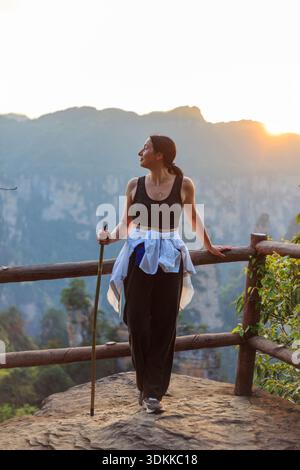 Une femme se tient sur un rebord de rocher avec un bâton de marche dans la main. Elle porte un débardeur noir et un pantalon noir. La scène est paisible et sereine, wi Banque D'Images