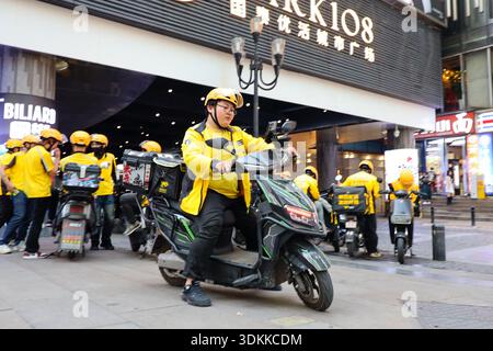 Chongqing Chine 4,7.2025. Courrier de livraison de nourriture chevauchant scooter électrique dans la rue animée de la ville Banque D'Images