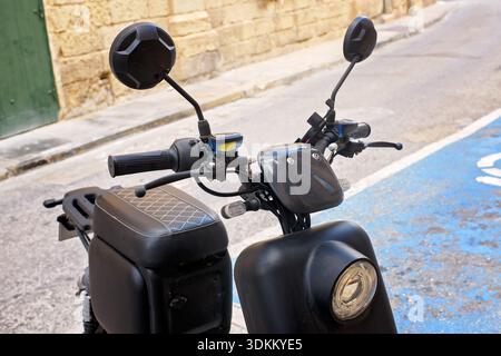 Sliema, Malte - 3 nov. 2025 : vue avant gros plan du guidon, du phare, des miroirs et du siège de scooter électrique noir dans une rue étroite. Banque D'Images