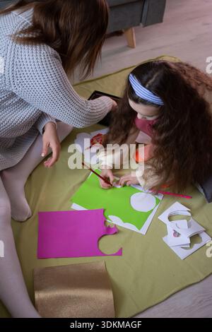 Deux individus, probablement une mère et un enfant, collaborent à un projet artistique. Ils utilisent divers papiers colorés, pochoirs et fournitures artistiques. L'activité se Banque D'Images